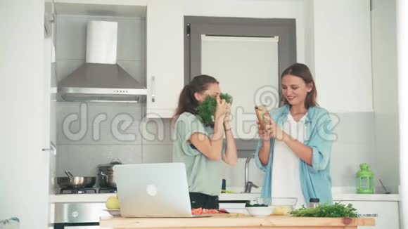 两个年轻漂亮的女人在厨房里用智能手机拍有趣的照片视频的预览图