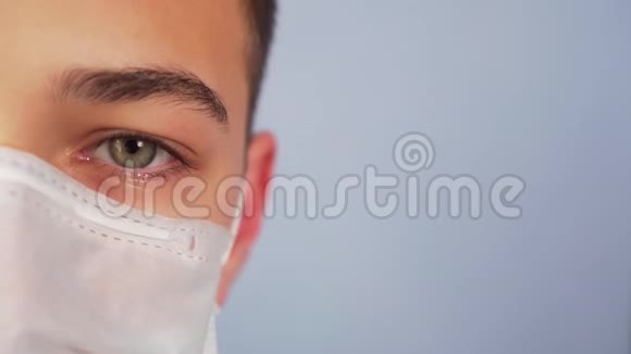 蓝色背景下戴医用防护面罩的年轻人的脸视频的预览图