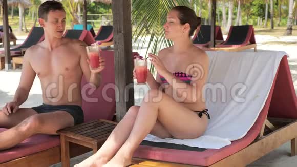 男人女人坐在日光浴床上在海滩上喝着鸡尾酒欢呼视频的预览图