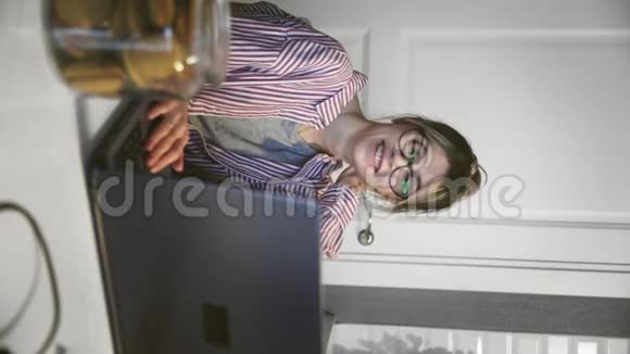 通过电话会议交流的年轻女性垂直视频在厨房里用笔记本电脑看电脑视频的预览图