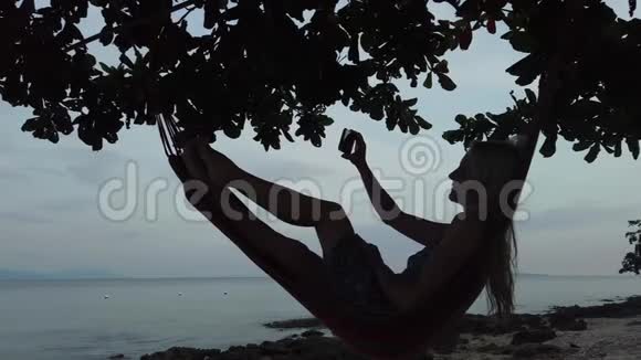 一个拿着电话躺在沙滩吊床上的女人视频的预览图