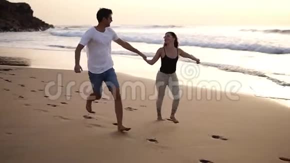 度假夫妇戴着太阳镜在海滩日落时浪漫地牵着手玩年轻一对相爱的情侣视频的预览图