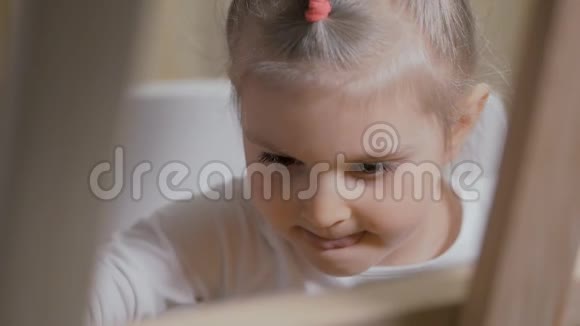 一位小女孩艺术家坐在画架前用画笔在画布上画画视频的预览图