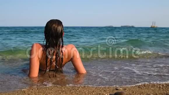 浅海中放松的美丽女孩波浪覆盖着她的身体海盗船的背景视频的预览图