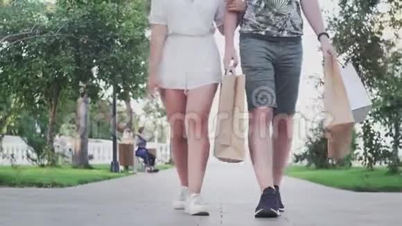 年轻可爱的一对夫妇手里拿着购物袋在夏季公园散步视频的预览图