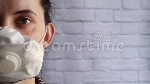 一个戴着医疗面具的沮丧的白种人年轻女子的半张脸紧闭着直视着镜头站在一个白色的里面前视频的预览图