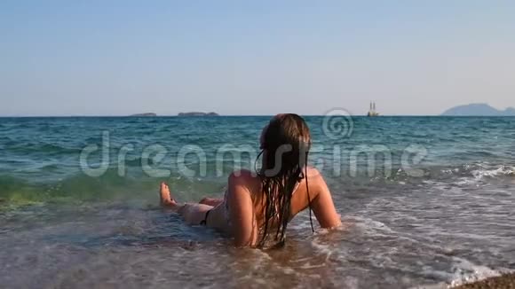 浅海中放松的美丽女孩波浪覆盖着她的身体海盗船的背景视频的预览图