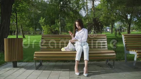 在夏天的公园里年轻的女人坐在长凳上手里拿着装满水果和蔬菜的棉网购物袋零废物视频的预览图