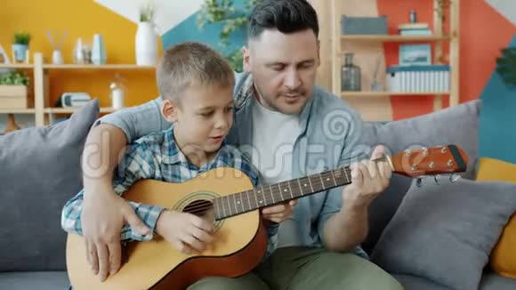 可爱的男孩在爱父的指导下在家学习吉他视频的预览图