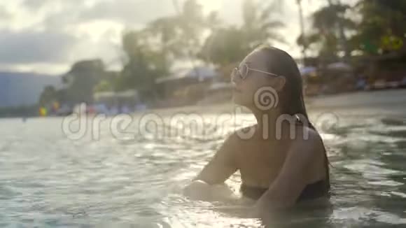 美丽的年轻女孩在苏梅岛海滩上享受大海中的日落戴着太阳镜和湿发的女孩视频的预览图