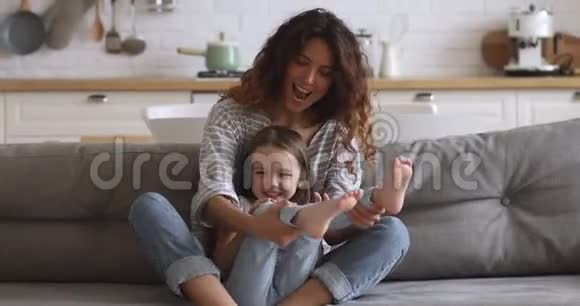 快乐的小妈妈和可爱的小女儿在沙发上玩耍视频的预览图