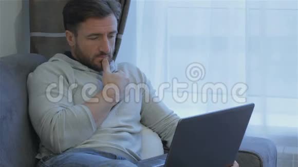 男人看着家里的笔记本电脑屏幕视频的预览图