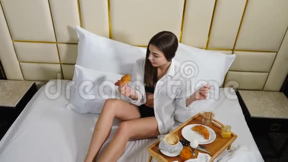 美丽的白种人女孩在床上用白色的床单和床上用品遮住阳光的肖像穿在黑暗中视频的预览图