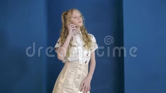 少女在蓝墙背景上用手机交谈年轻漂亮的女人用智能手机视频的预览图