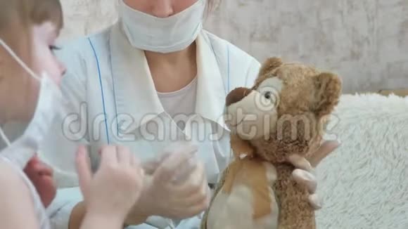 可爱的女孩给玩具熊打针婴儿戴着医用面具玩耍孩子在医院玩游戏假装是视频的预览图