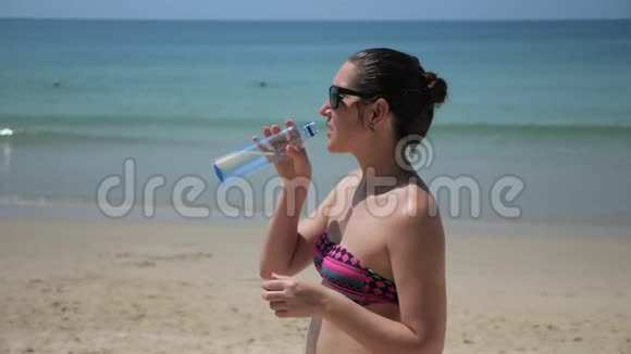 布鲁内特女士站在海滩上从瓶子里喝水视频的预览图