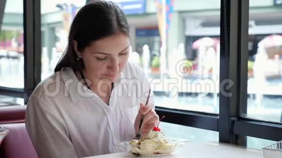 穿着白色衬衫的布鲁内特在咖啡馆的餐桌上吃冰淇淋视频的预览图
