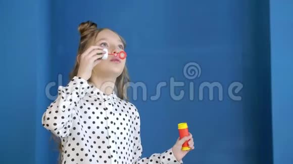 浪漫的少女在工作室的蓝色背景上吹肥皂泡漂亮的少女吹泡泡肥皂视频的预览图