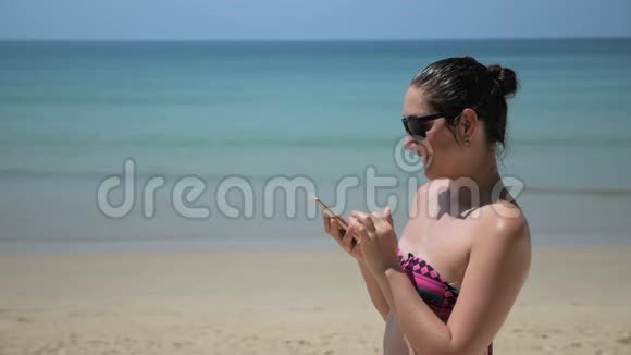 女孩站在海滩上用智能手机上网冲浪视频的预览图