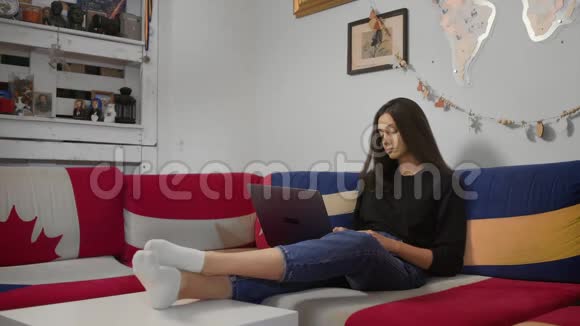 严肃的年轻女子在笔记本电脑上打字在网上聊天使用应用程序坐在家里的沙发上视频的预览图