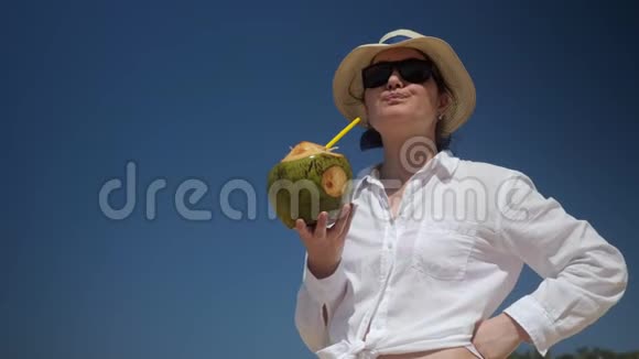 女士站着在蓝天上用吸管喝椰子视频的预览图
