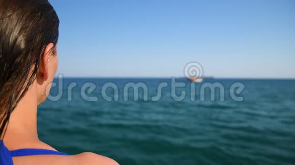 美丽的女孩在游泳套间看着一艘船在海上视频的预览图