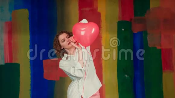 迷人的女孩金发卷发手持红色气球在相机摆姿势穿着红色气球的滑稽女人视频的预览图