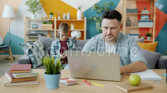父亲的自由职业者用笔记本电脑工作然后和儿子可爱的孩子在家交谈视频的预览图