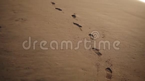 追踪海滩金色潮湿沙滩上脚印的特写镜头视频的预览图