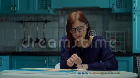年轻的30多岁的女人用画笔缓慢地坐在厨房的家里画彩色图片孤独的绘画爱好视频的预览图