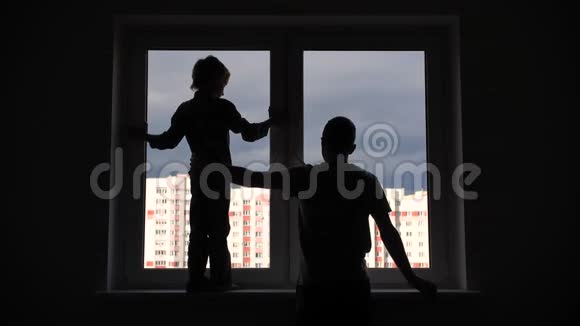 一位父亲和他的儿子在公寓窗户的背景下的剪影视频的预览图