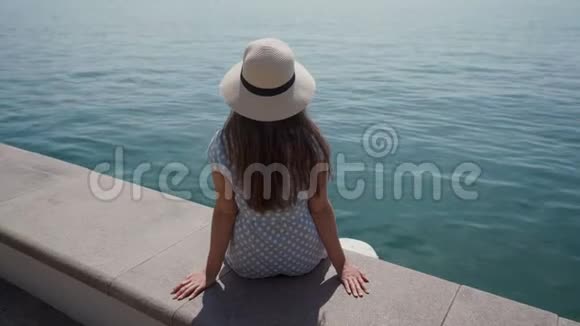 阳光明媚戴帽子的女人坐在湖边的石墩上放松视频的预览图