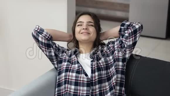检疫期间厨房里的年轻女子女孩坐在沙发上交叉的手臂在头后微笑享受休息时间视频的预览图