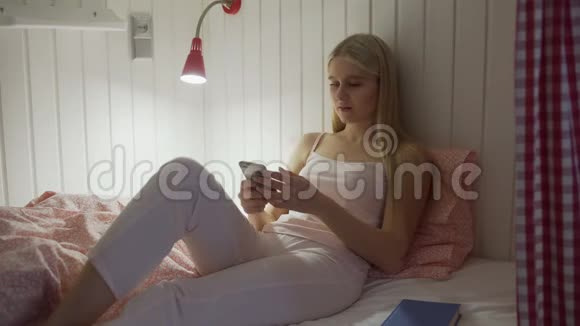 一个年轻漂亮的女人坐在宿舍房间的床上用完智能手机睡觉视频的预览图