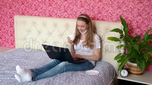 在家远程工作一个漂亮的白种人女孩正在卧室里的笔记本电脑上工作床上躺着一张保护性医疗设备视频的预览图