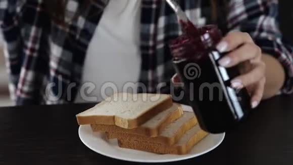 检疫期间厨房里的年轻女子用叉子把红果酱涂在面包上的女人的动作甜蜜甜蜜视频的预览图