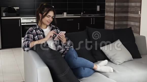 检疫期间厨房里的年轻女子女孩坐在沙发上在智能手机上打字在线社交媒体微笑时视频的预览图