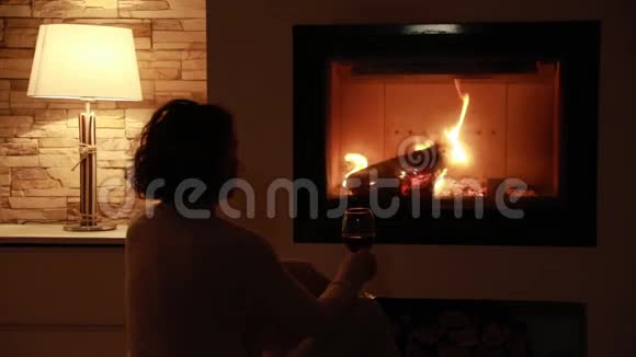 年轻女子坐在家里燃烧的壁炉旁视频的预览图