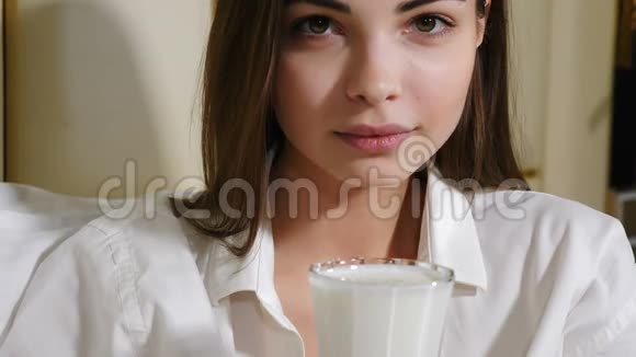 迷人的年轻女子微笑着看镜头喝牛奶或其他牛奶饮料的肖像一个漂亮的女孩视频的预览图