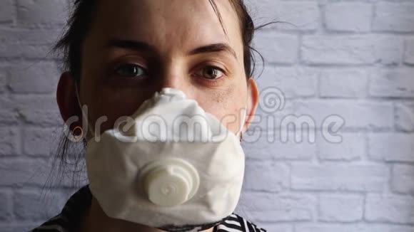 一位戴着面具的年轻女子在白色砖墙上的冠状病毒疫情中的肖像Covid19健康和安全概念视频的预览图