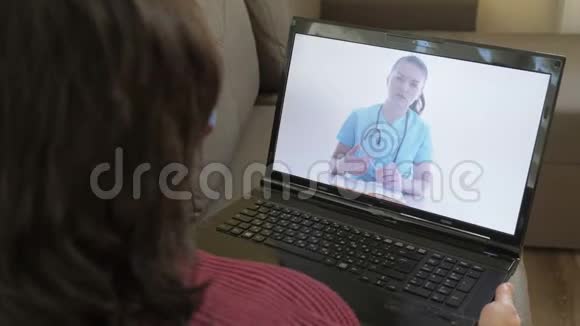 在线医生坐在公寓沙发上用笔记本电脑的女人通过互联网咨询她的医生视频的预览图