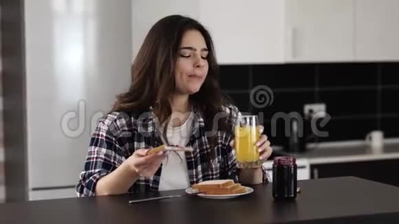 检疫期间厨房里的年轻女子女孩用果酱和微笑吃面包性格开朗的女性喝橘子视频的预览图