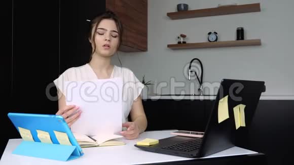 检疫期间厨房里的年轻女子女孩坐在桌子旁手里拿着文件在笔记本电脑键盘上打字工作视频的预览图