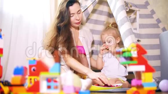 年轻的孕妇和她的女儿在家里的玩具帐篷里吃浆果视频的预览图