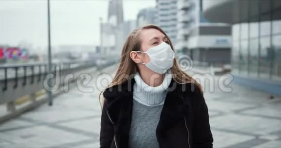 COVID19流行病保护年轻的金发女郎戴着医用口罩在封锁期间沿着空城街道散步视频的预览图