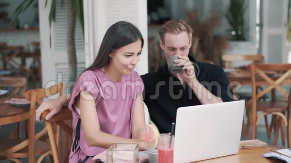 时尚咖啡馆里的男人和女孩使用笔记本电脑喝咖啡笑有趣的视频视频的预览图