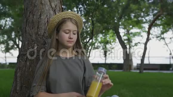 戴着草帽在户外夏天公园喝橙汁的年轻女孩视频的预览图