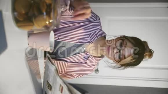 年轻漂亮的黑发女人带着眼镜喝咖啡吃饼干在家里看报纸的垂直视频视频的预览图