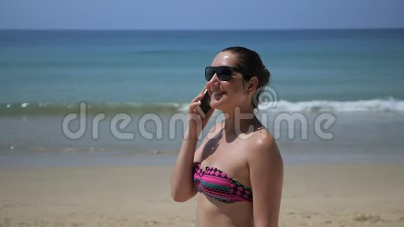 穿比基尼的女孩在海滩上的智能手机上聊天视频的预览图