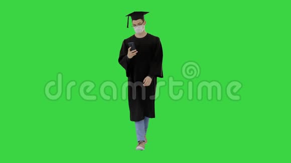 带着毕业礼服的年轻人戴着医疗面具在绿色屏幕上使用智能手机Chroma键视频的预览图
